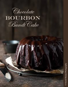 a bundt cake with chocolate icing on a plate next to a knife and fork