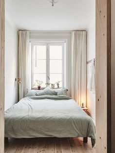 a bed sitting under a window next to a wooden floor covered in blankets and pillows