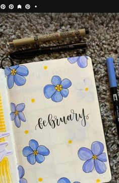 an open notebook with blue flowers and writing on the cover, next to two markers