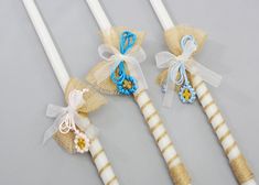 three white candles decorated with blue and yellow flowers, tied in burlap bags