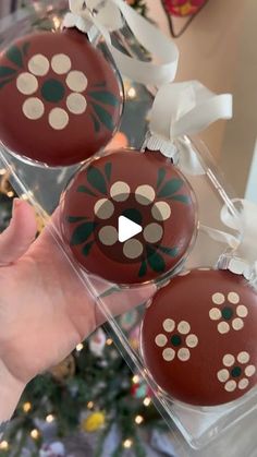 someone is holding two chocolate ornaments in front of a christmas tree with decorations on it