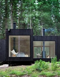 a black cabin in the woods with two chairs