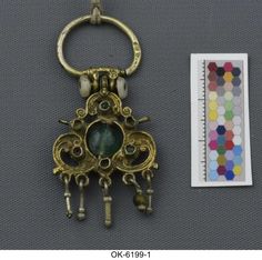 a gold keychain with a green stone in the middle and a ruler next to it