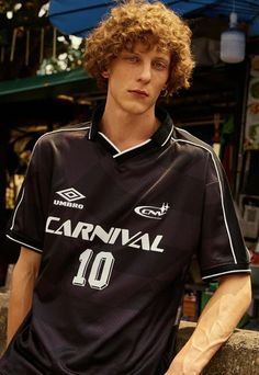 a young man with curly hair wearing a black soccer jersey and holding his hands in his pockets