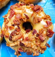 a doughnut covered in bacon sitting on top of a blue plate next to other donuts