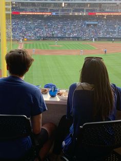 two people sitting at a table watching a baseball game from the stands in an empty stadium