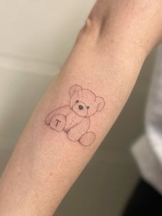 a small teddy bear tattoo on the left forearm and arm, with an i in it's center