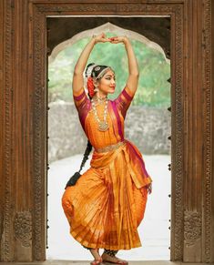 a woman in an orange and pink dress doing a dance pose with her hands up