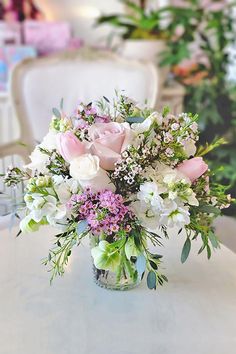 a vase filled with lots of flowers on top of a white table next to a chair