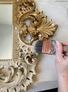 a person is holding a paintbrush and painting a gold frame on a white wall