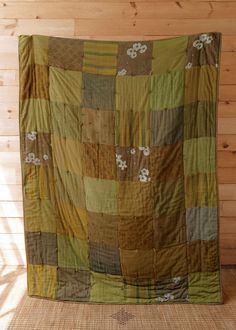 a large green and brown quilt sitting on top of a wooden floor next to a wall