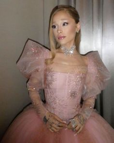 a woman in a pink dress is standing next to a wall and wearing a tiara