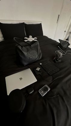 a bed with black sheets and accessories on it, including an apple laptop sitting on top of the bed