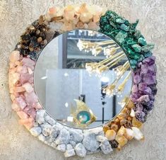 a circular mirror with many different colored rocks around it and the reflection of a gold chandelier