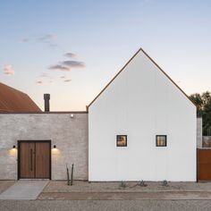 a white house with two doors and windows on the outside, along side a brick wall