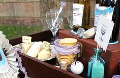 an assortment of wine, cheese and crackers in a wooden box on a picnic table