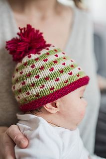 a woman holding a baby wearing a knitted hat with pom - poms