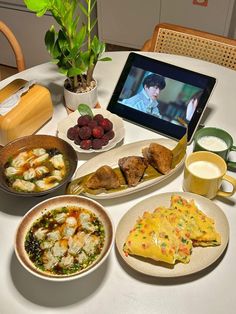 a table topped with plates and bowls filled with food next to a laptop computer on top of a white table