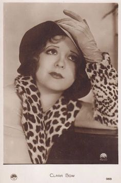 an old photo of a woman wearing a hat and leopard print coat with her hands on her head