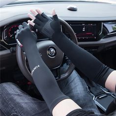 a person in black gloves driving a car with their hands on the steering wheel and wearing an arm warmer