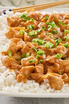 a white plate topped with rice covered in chicken and green onions next to chopsticks