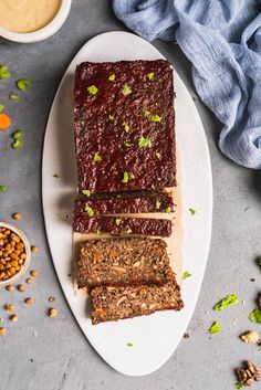 slices of meatloaf on a plate with nuts and sauces around it next to a blue towel