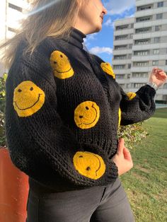 a woman wearing a black sweater with yellow smiley faces drawn on it's sleeves