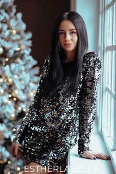 a woman standing next to a christmas tree in front of a window with the words estherlabella on it