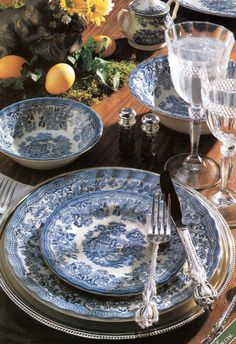 blue and white plates with silver trim sit on a wooden table next to yellow flowers