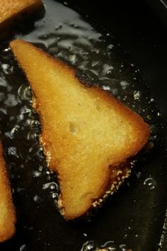 three pieces of bread frying in oil on a black skillet with water droplets