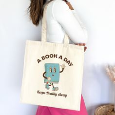 "Introducing our whimsical canvas tote bag, adorned with a charming vintage book mascot cartoon and the delightful slogan \"A book a day keeps reality away.\" Crafted for book lovers who appreciate both style and wit, this sturdy tote is perfect for carrying your literary essentials with a touch of literary charm. Embrace your love for reading and make a statement wherever you go! 📚 This 100% cotton bag comes in one size - 15\" x 16\"- perfect for everyday wear. The bag features 20\" handles (made from the same canvas), making it easy to carry even with a week's worth of shopping. .: 100% cotton canvas .: Heavy fabric (12 oz/yd² (406.9 g/m .: Sewn-in label" Canvas Bag For Back To School Gift, Back To School Canvas Bag Gift, Rectangular Canvas Bag With Bookish Style, Bookish Rectangular Canvas Bag, Vintage Rectangular Canvas Bag As Gift, Retro Canvas Bag As A Gift, Bookish Bags With Letter Print For Gift, Gifts For Book Lovers, Book Bags