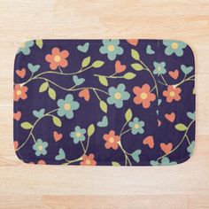 a bath mat with flowers on it sitting on top of a wooden floor next to a wall