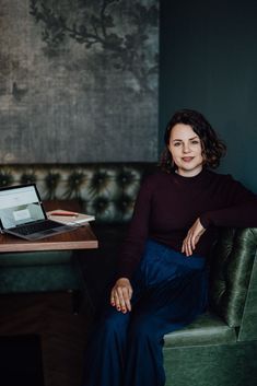 a woman sitting on a green couch in front of a table with a laptop computer