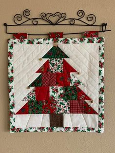 a quilted christmas tree hanging on a wall with a metal rack above it that has a red, green and white patchwork design