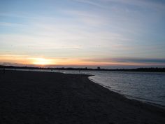 the sun is setting at the beach with people walking on it