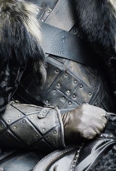 a close up of a man in armor with fur on his head and hands resting on his chest