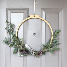 a wreath with pine cones and greenery hanging on a door