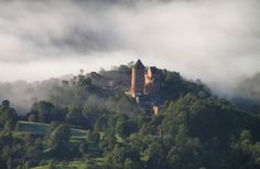 a castle sits on top of a hill surrounded by trees and fog in the distance