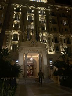 the hotel carlton is lit up at night with its lights on and people walking in front