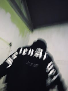 a blurry image of a person in a black hoodie standing next to a wall