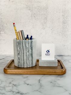 a marble pen holder with pens and pencils in it sitting on a wooden tray