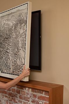 a woman is holding up a framed map on a fireplace mantel in front of a brick wall