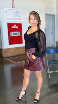 a woman is posing for the camera in a black top and brown leather miniskirt