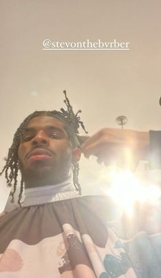 a man getting his hair cut by another person in front of him with the sun shining behind him