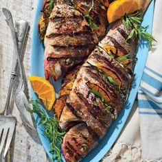 grilled fish on a blue plate with orange slices and herbs next to it, along with silverware