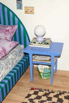 a small blue table sitting next to a bed on top of a hard wood floor