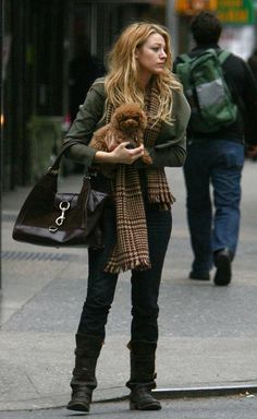 the woman is walking down the street with her teddy bear in her hand and looking at something