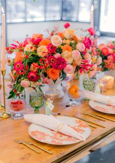 a wooden table topped with plates and glasses filled with oranges, pinks and red flowers