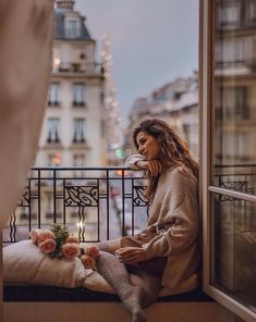 a woman sitting on a window sill looking out at the city