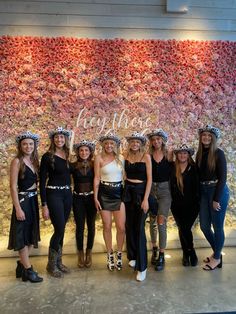 a group of women standing next to each other in front of a wall with flowers on it